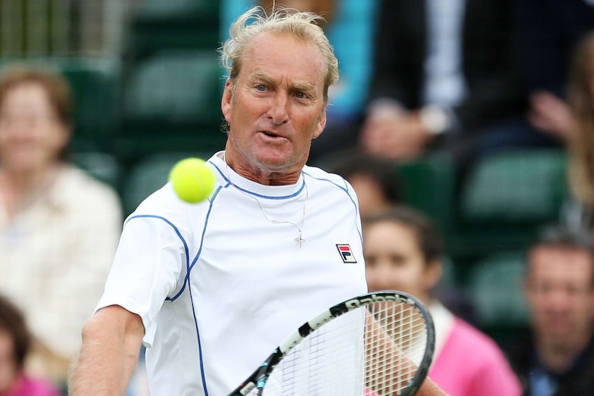 Peter McNamara lines up a shot with a racquet on a tennis court.