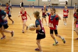 Junior netballers play on an indoor court