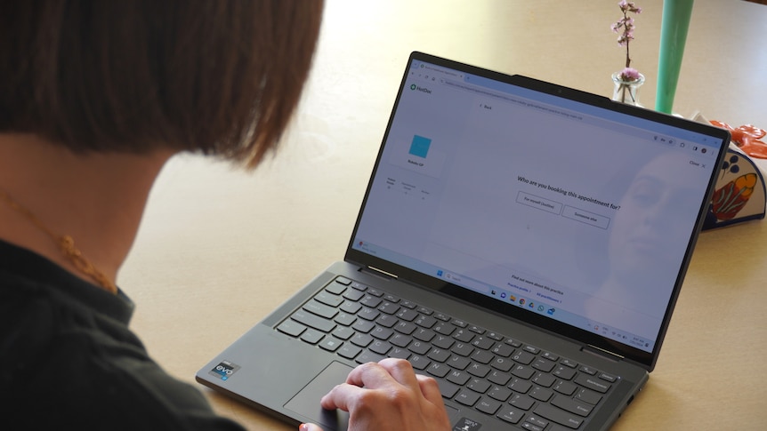 Woman with brown short hair scrolls on her laptop booking an appointment with her GP.