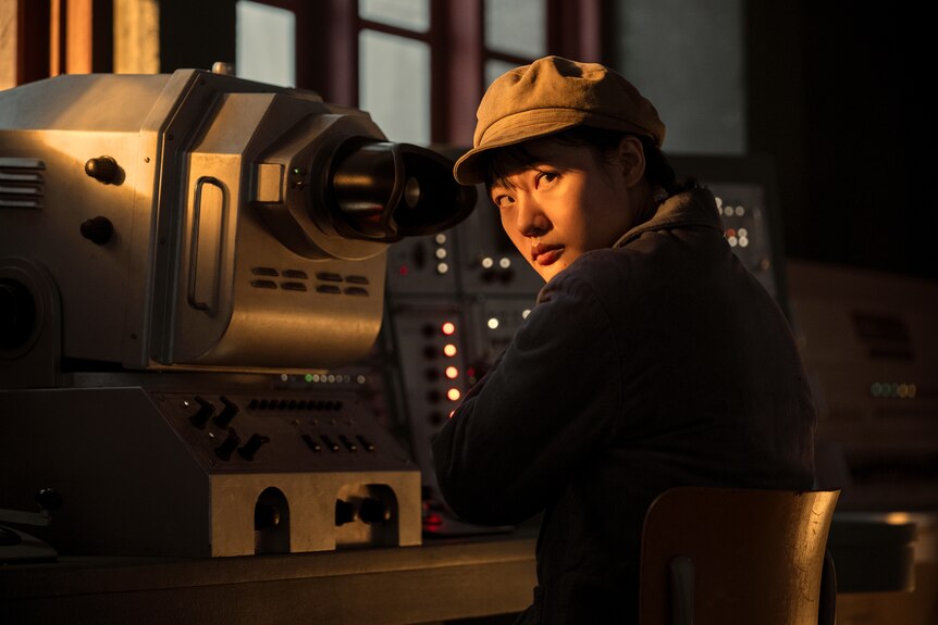 A close up of a woman wearing a cap in front of a machine under the glow of a light.
