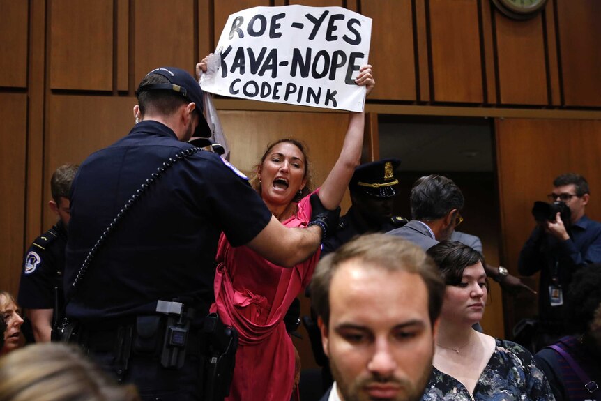 A protester holding a sign is escorted out of Brett Kavanaugh's Senate confirmation hearing.