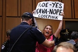 A protester holding a sign is escorted out of Brett Kavanaugh's Senate confirmation hearing.