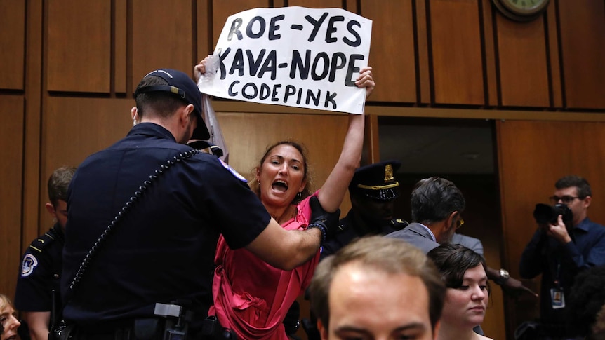 A protester holding a sign is escorted out of Brett Kavanaugh's Senate confirmation hearing.