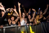 A group of young people dance behind a barricade at a music event