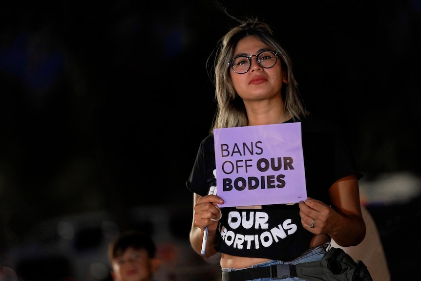 A woman holds a sign that says bans off our bodies 