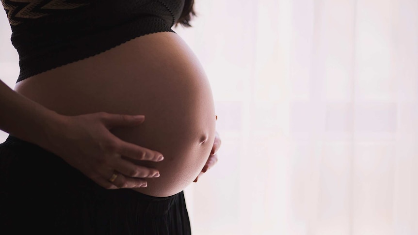 Close-up of woman holding her pregnant stomach for a story about reproductive abuse and what to do about it.