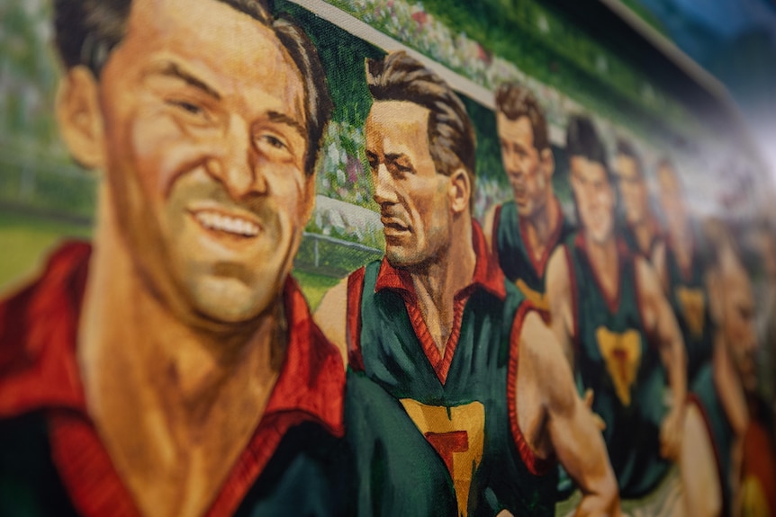A close-up of a painting shows a man running on to a field in an AFL jersey.