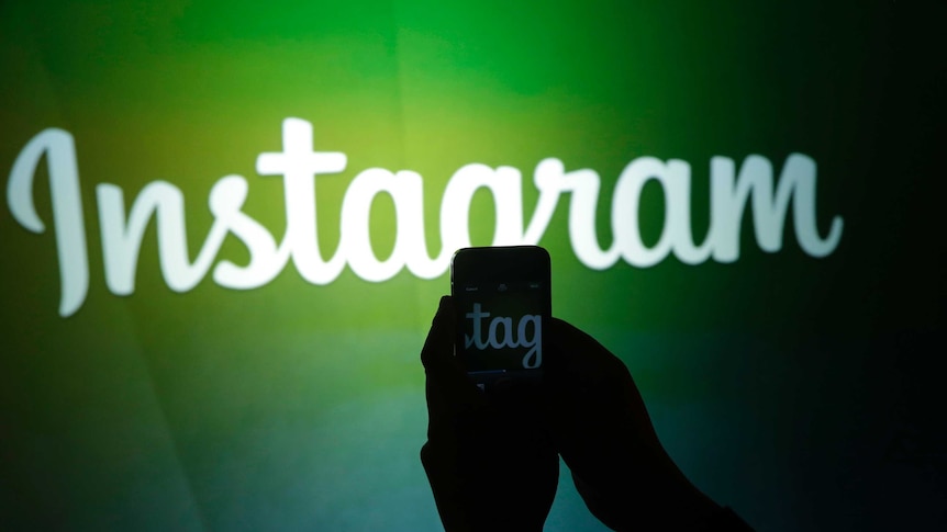 A person taking a photo of a green wall with a written logo of Instagram in white.