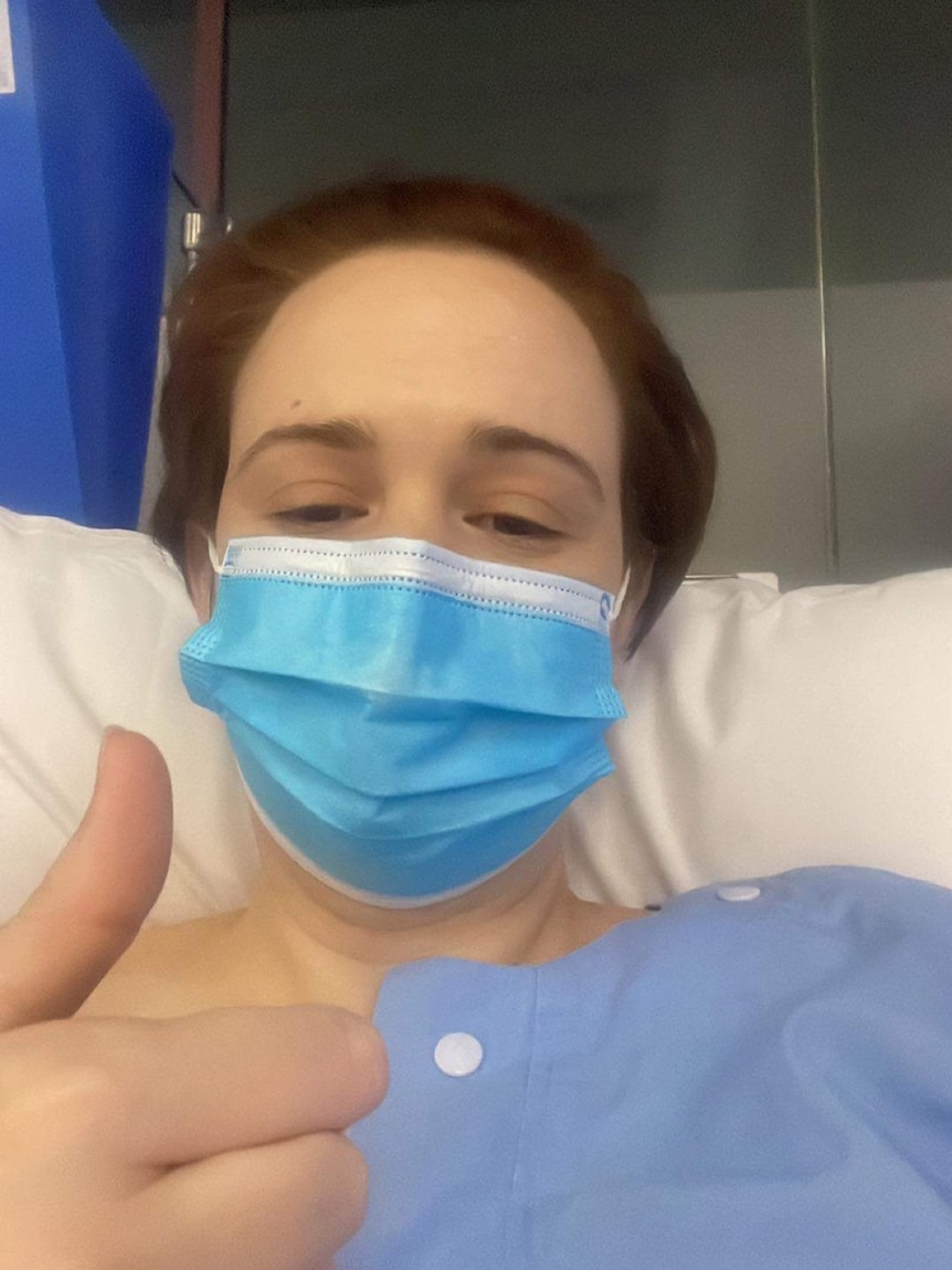 Clare Negus sitting in a hospital bed showing the thumbs up.