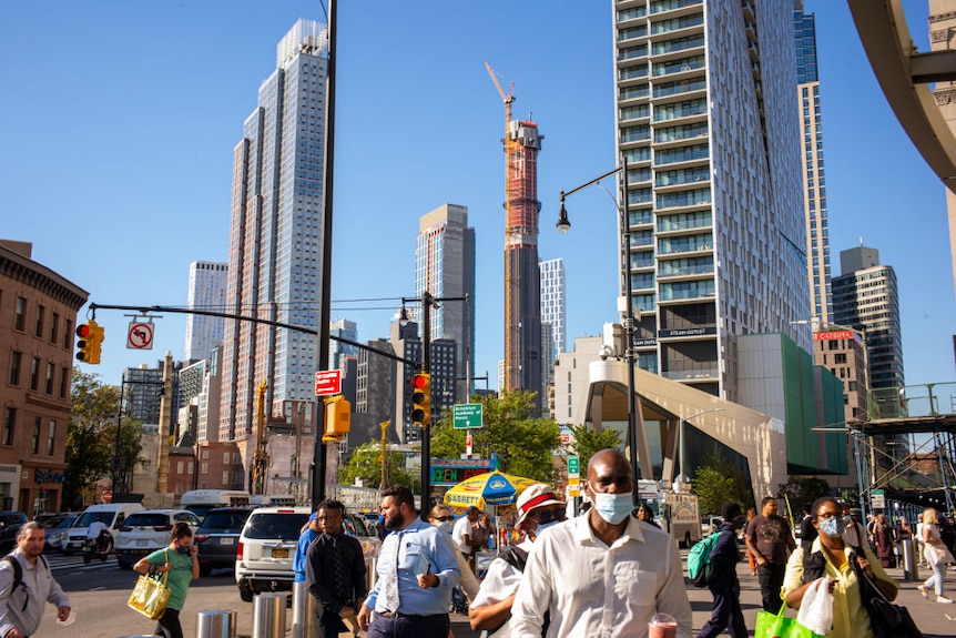 People walk in a street as a skyscraper is under construction in the background.