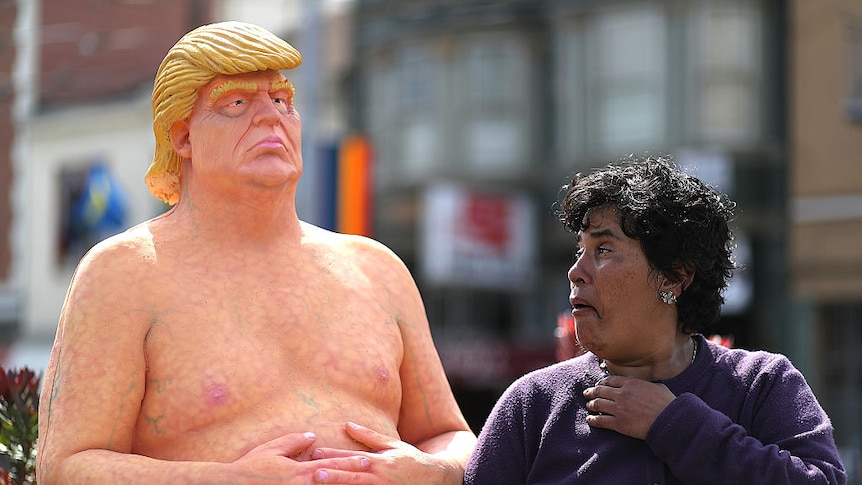 A passerby looks at a statue depicting Donald Trump in the nude.