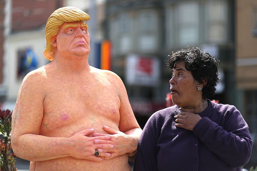 A passerby looks at a statue depicting Donald Trump in the nude.
