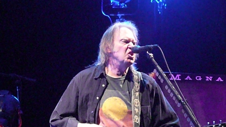 Neil Young performs while wearing a T-shirt displaying the Aboriginal flag