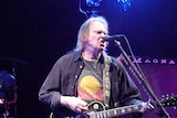 Neil Young performs while wearing a T-shirt displaying the Aboriginal flag