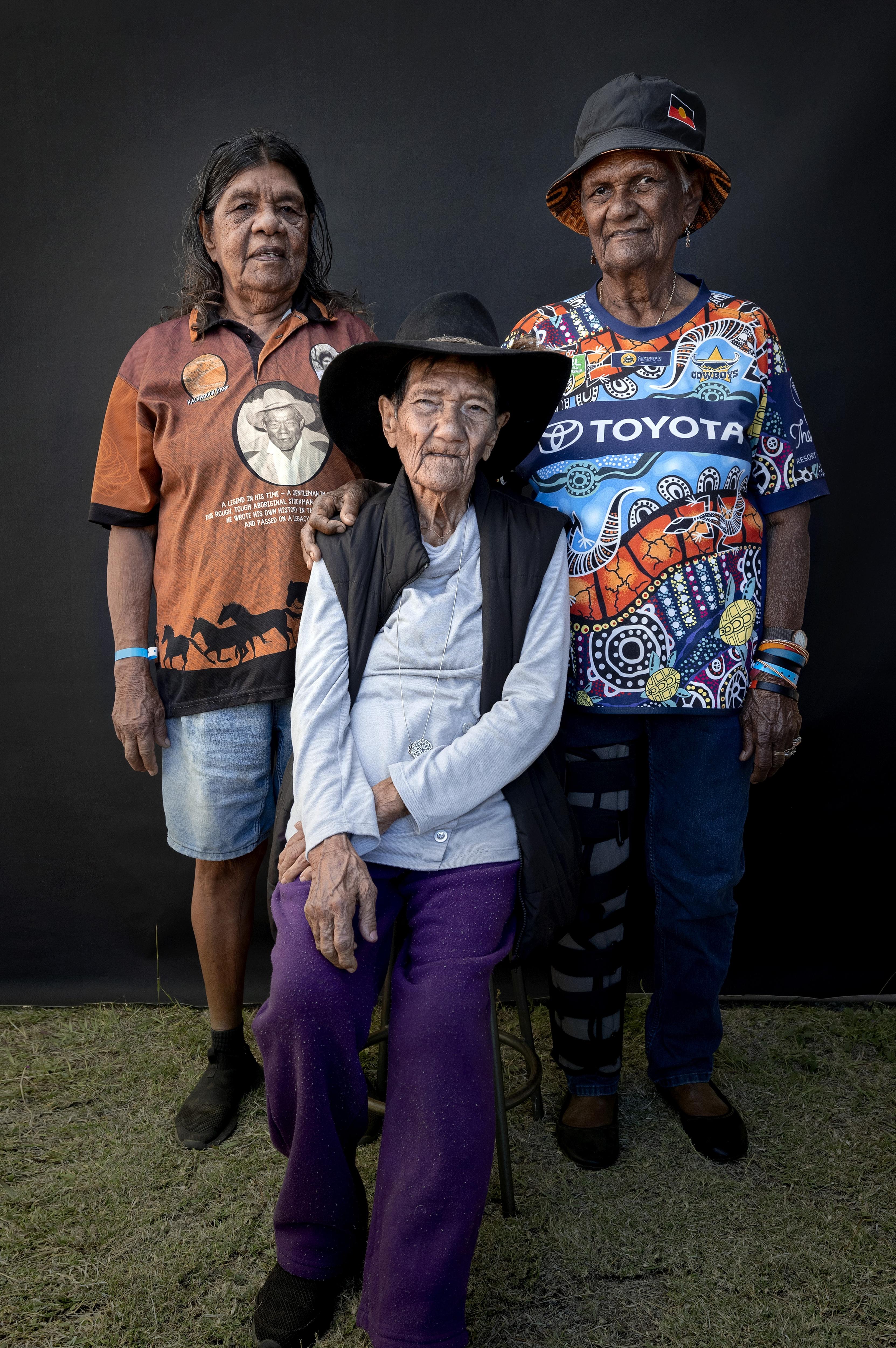 3 generations of indigenous woman, two stand one sits in the middle