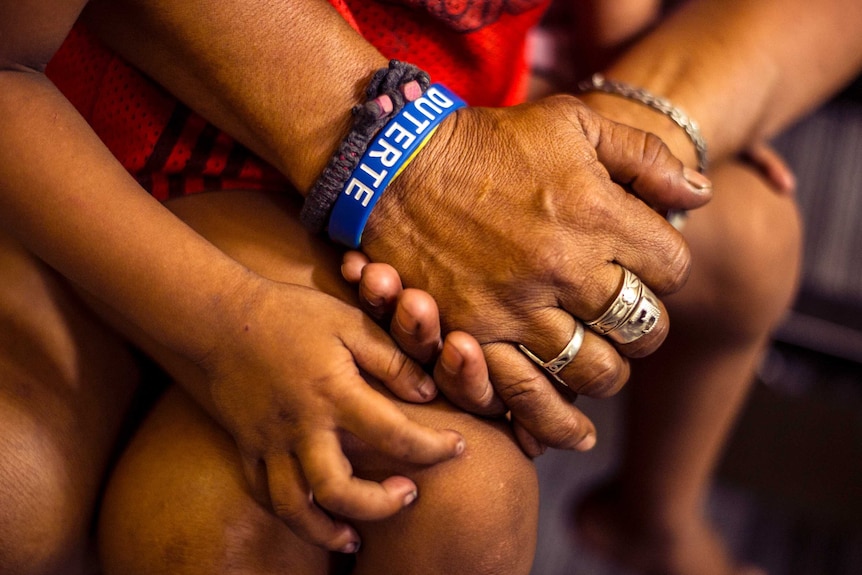 A woman wearing a Duterte wristband accompanies her son at a police station after being detained for violating a curfew.