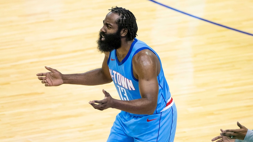 James Harden looks frustrated, leaning forward and holding his arms out in front of him, wearing a baby-blue singlet