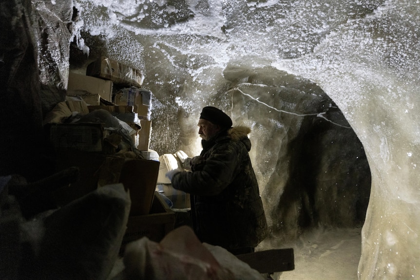 a man sits inside an ice cave underground looking through boxes