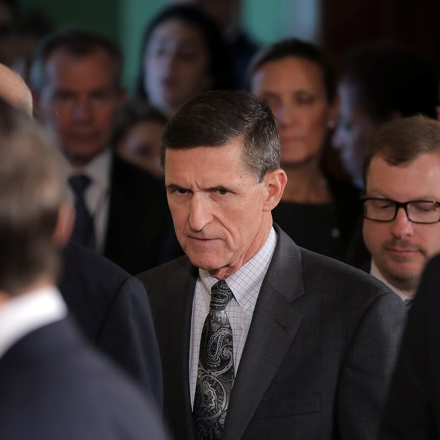 Michael Flynn walking while surrounded by officials.
