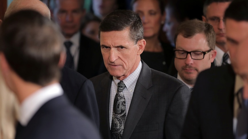 Michael Flynn walking while surrounded by officials.