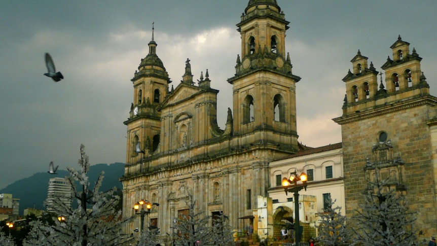 A sandstone classical cathedral is pictured in front of fake white Christmas trees set against a stormy sky.