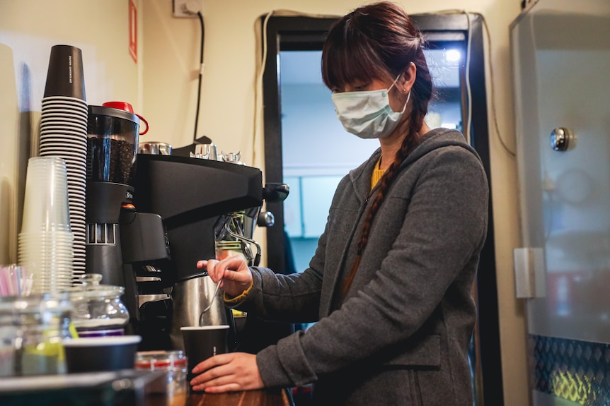 A woman wearing a mask puts tea in a cup