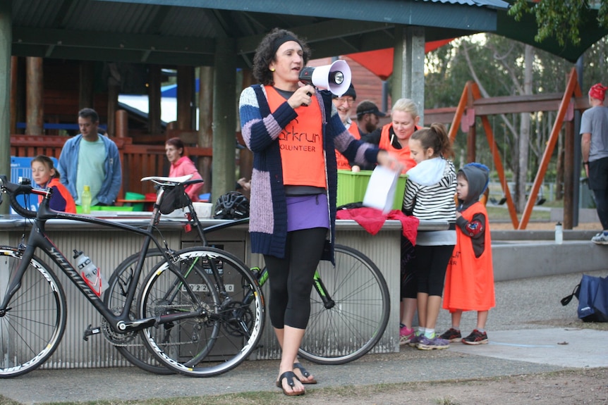 Ada habla por un megáfono en parkrun mientras la gente se reúne y escucha.