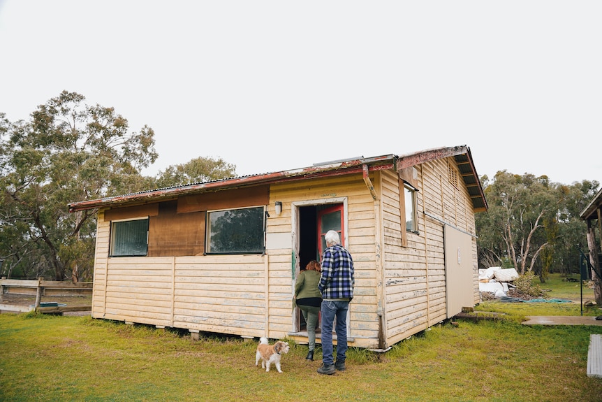 A man walks into a small weatherboard building on an overcast day.