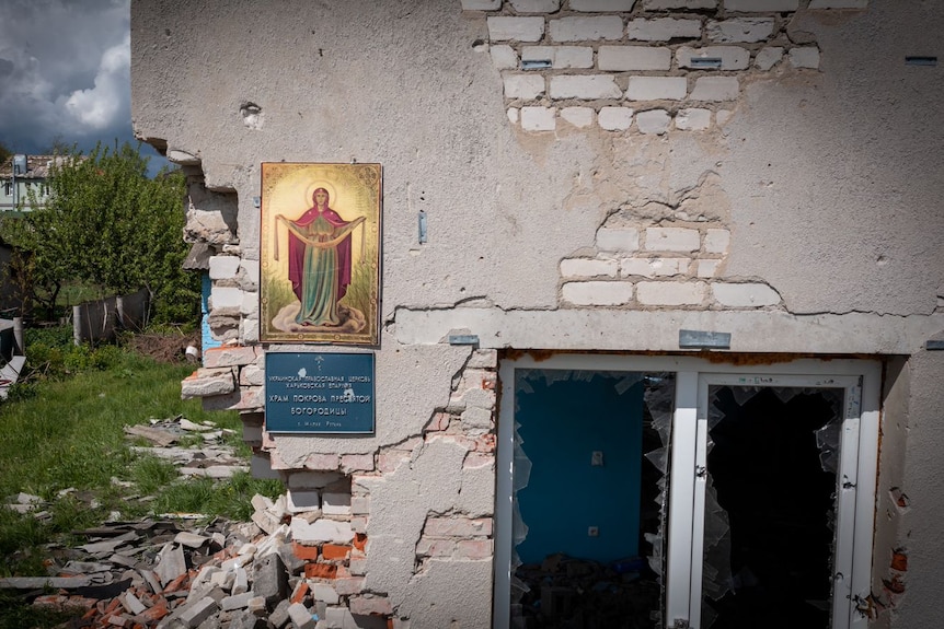 A painting of the Virgin Mary stuck to an external wall with bricks crumbling away, a smashed window