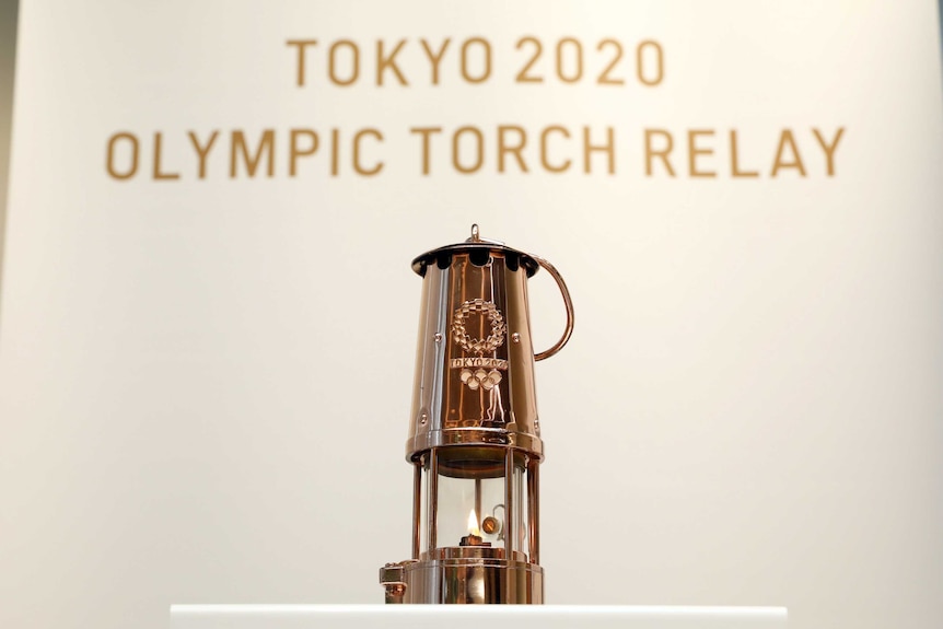 The flame for the 2021 Tokyo Olympic Games burns in a lantern in front of a sign reading Tokyo 2020 Olympic Torch Relay.