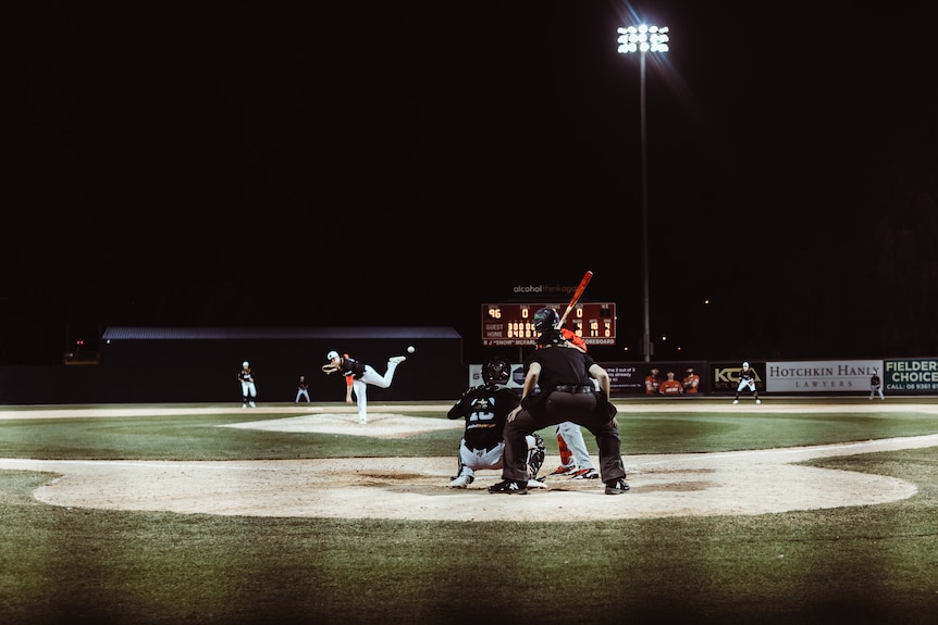 A baseball game captured from behind home plate, with the ball in mid-air after it was pitched towards a batter.