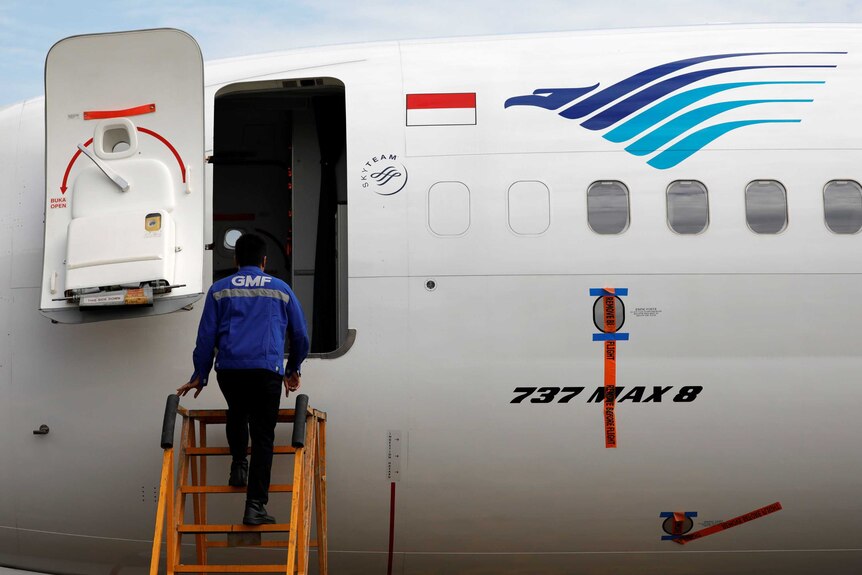 A technician climbs stairs to enter a grounded Boeing 737 MAX 8 plane.
