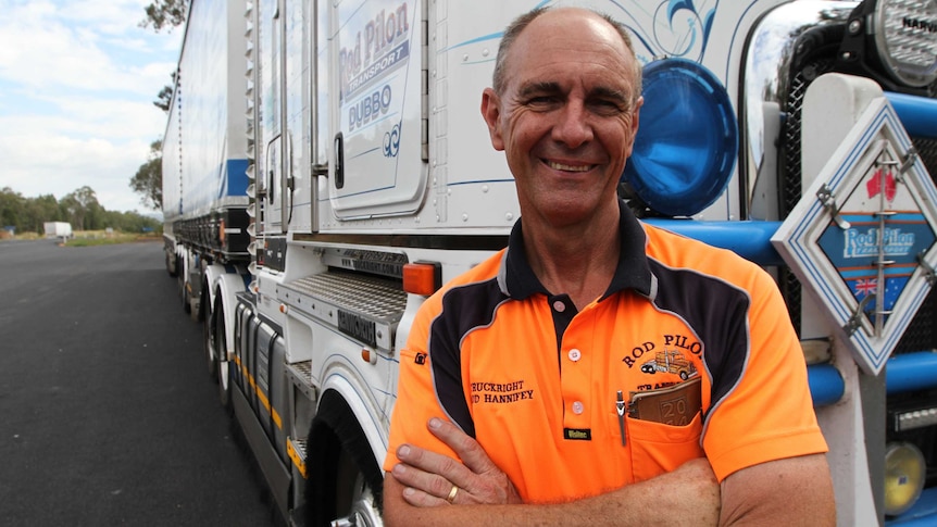 A truck driver in high-viz vest smiles in front of his truck