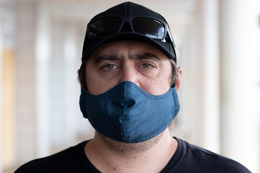 a man wearing a cap and face mask stares at the camera