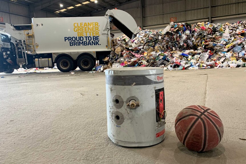 A small hot water cylinder and a basketball sitting in front of a pile of rubbish