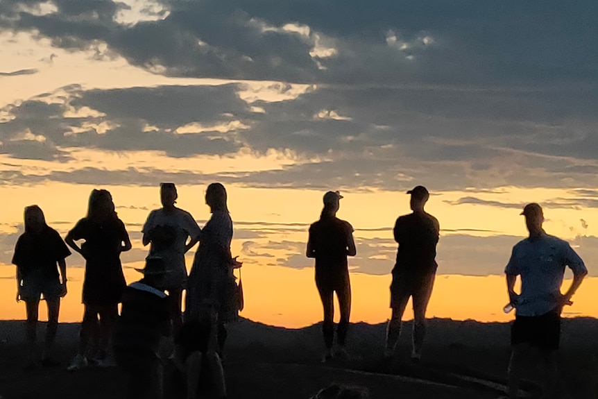 people in shadow stand on cliff edge with sun setting behind them