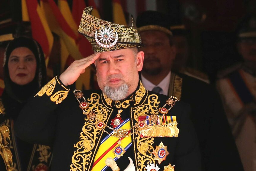 Malaysian King Sultan Muhammad V is wearing elaborate royal dress in gold and black and giving a salute
