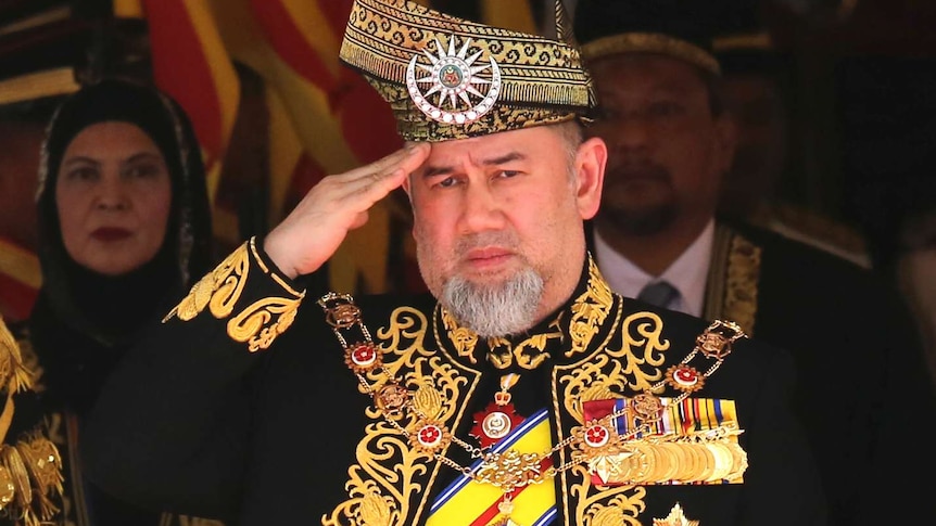 The former Malaysian sultan wearing a traditional outfit and saluting.