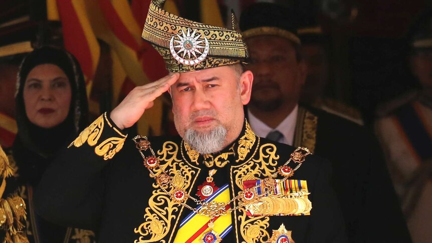 Malaysian King Sultan Muhammad V is wearing elaborate royal dress in gold and black and giving a salute