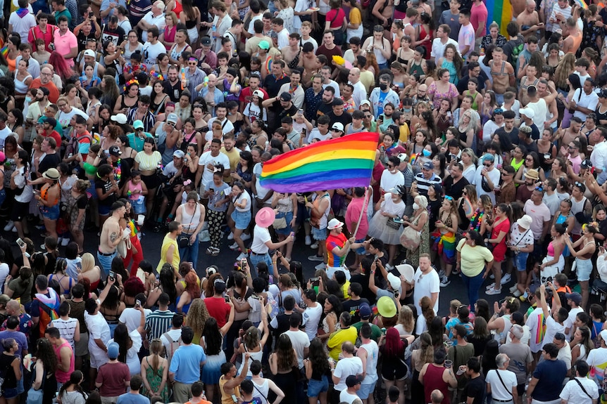 a person holds up a rainbow pride flag as they walk through a crowd of people