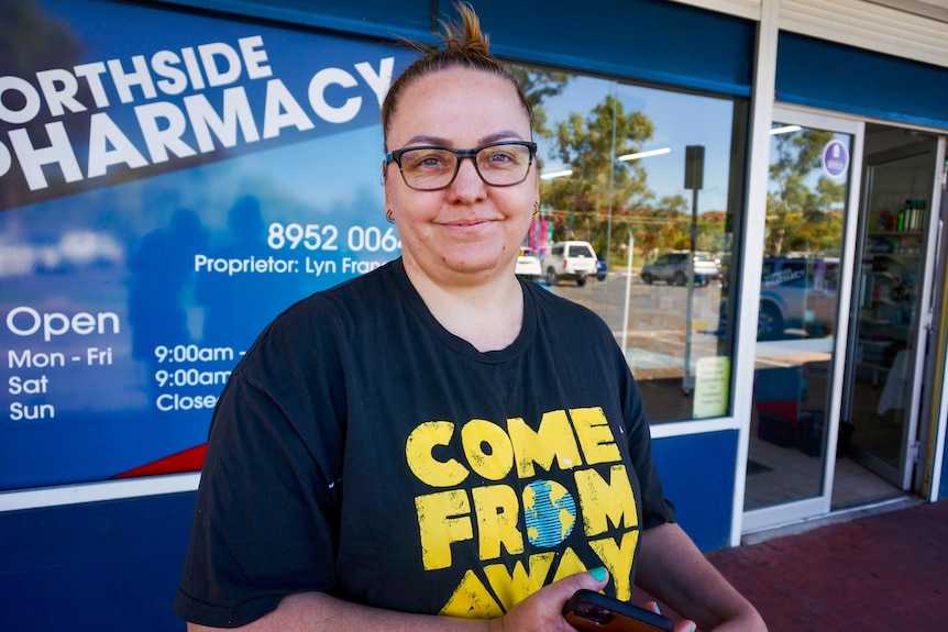 Woman stands in front of a pharmacy and smiles