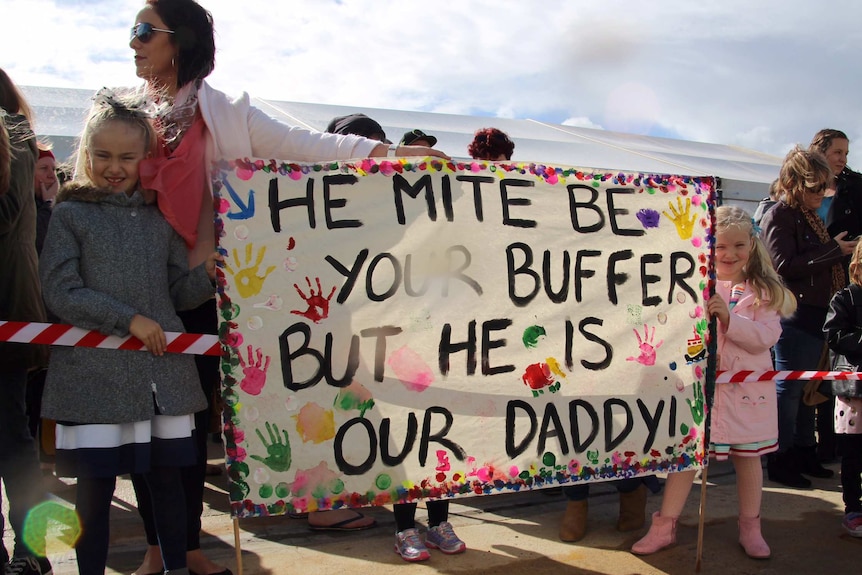 Two girls and their mum hold a brightly coloured banner.