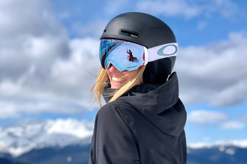 A woman in a ski helmet and goggles poses for a photo