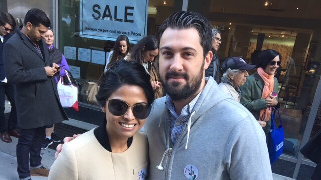 A woman and man wear "I voted" stickers outside a polling booth.