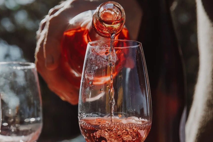 Rose wine being poured from a bottle into a wine glass. Only the hand of the person pouring it is visible.