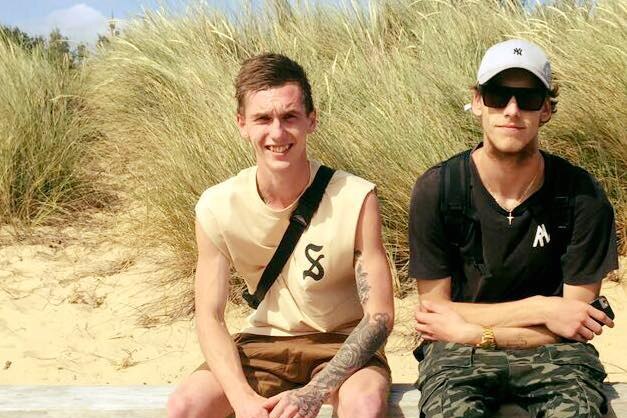Two young men sitting on a sand dune smiling.
