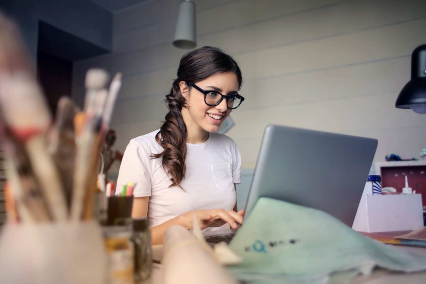 A young woman in a mentally healthy work place smiles while reading from her laptop screen.