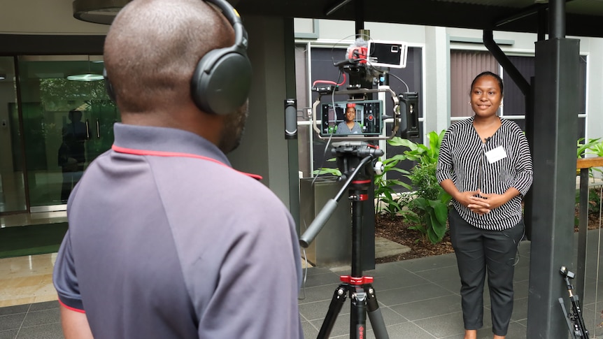 A woman standing in front of a camera with a microphone in her hand