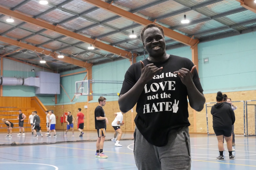 A man does the 'shaka' sign with his hands, and has a t-shirt which reads 'spread the love not the hate'