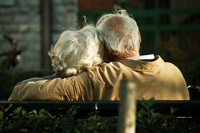 An elderly couple sits on a park bench.